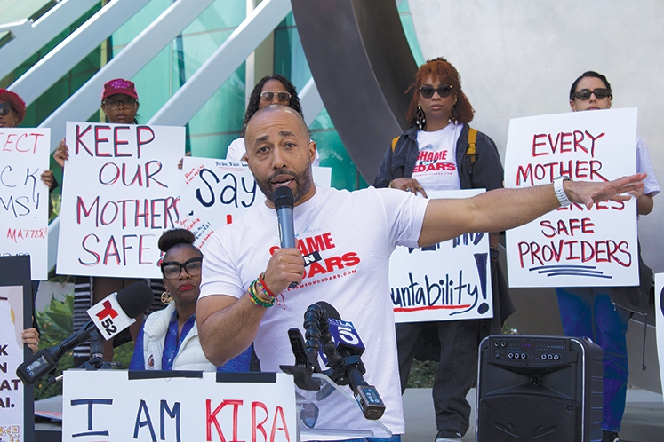 Charles leading rally with Keep Our Mothers Safe protest signs